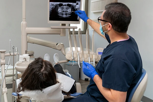  A dentist pointing at an xray on a computer monitor with a patient in a chair